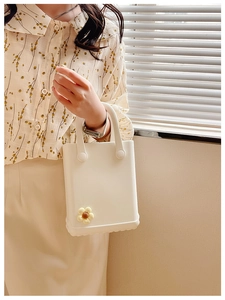 Detail einer weißen EVA-Strandtasche mit gelber Blume, gehalten von einer Frau im Kleid