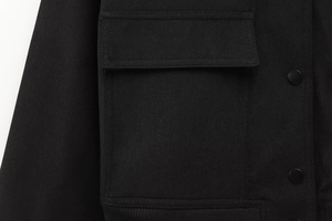 Makrodetail einer schwarzen Jacke mit Köperstoffstruktur und Metalldruckknopfverschluss