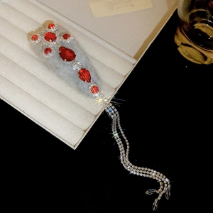 Detail of red rhinestone cross hair clip with long silver tassels on velvet box