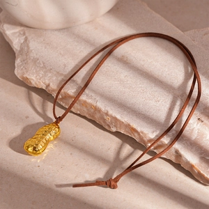 Detailed view of a textured golden peanut pendant on a brown cord against light stone