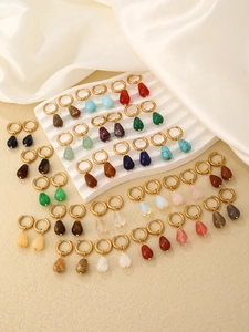 Detail of colorful teardrop stone earrings with polished gold hoops on beige display
