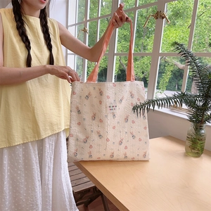 Detail of light beige canvas tote bag with floral rabbit pattern and woven pink straps