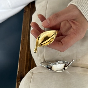 Detail showing leaf-shaped rings in gold and silver finish with smooth metallic texture