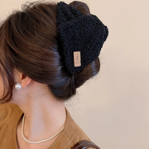 Detail van een zwarte pluche haarklem met leren label in golvend haar gedragen