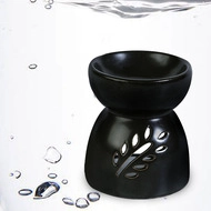 Black ceramic oil burner with leaf cutouts splashing in clear water, macro detail view