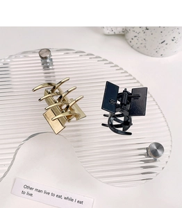 Detail of square gold and black metal hair claws displayed on a modern acrylic stand