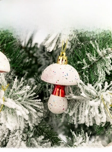 Close-up of mushroom Christmas ornament with colorful dots hanging on a snowy pine branch