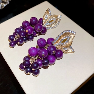 Détail macro de boucles d'oreilles raisins violets avec feuilles dorées et zircons