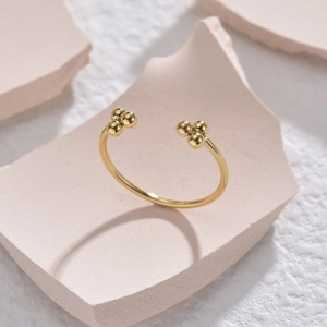 Anello aperto regolabile dorato con grappoli di sfere su uno sfondo materico elegante