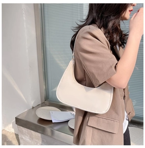 Side view of cream nylon crescent hobo bag worn by a model in a minimal urban setting