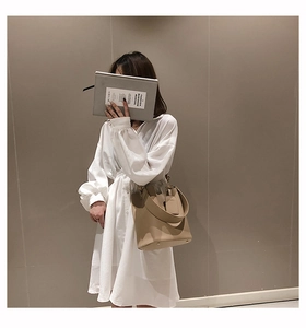Detail of beige bucket bag with metal studs and wide strap on white dress