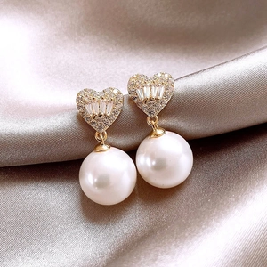 Close-up of heart-shaped pearl earrings with gold base on luxury champagne satin