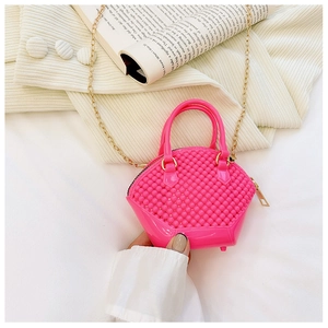 Pink jelly mini shell bag with bubble texture and golden chain held over a book