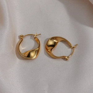 Irregular twisted gold hoop earrings with metallic luster on white satin background