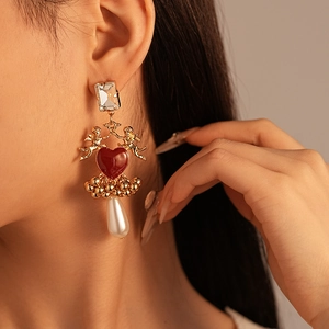Détail macro de boucles d'oreilles baroques avec cupidon doré, cœur rouge et perle