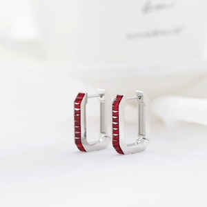 Detailed macro view of silver huggie earrings with rectangular red zircon stones