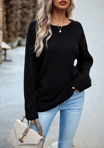 Dettaglio del maglione nero a girocollo con elegante trama a trecce sulle maniche lunghe