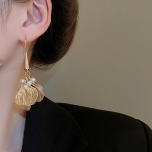 Detail of golden leaf earrings with white pearls worn by a model in a black suit