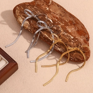 Detailed shot of gold and silver bow tassel earrings on a wooden decorative stand