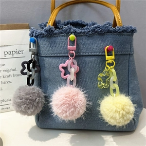 Detail of gray pink and yellow plush ball pendants hanging on a blue denim bag