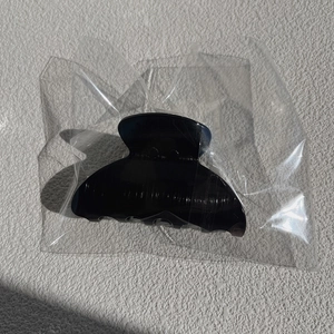 Detail of shell-shaped large black hair claw clip in clear plastic packaging