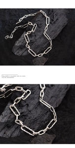 Macro detail of silver rectangular link chain with textured surface on black charcoal
