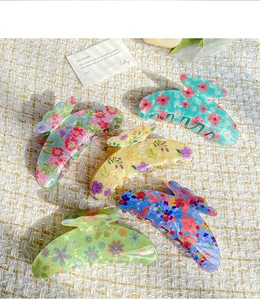 Close-up of floral acetate hair claws in various colors on a beige woven background