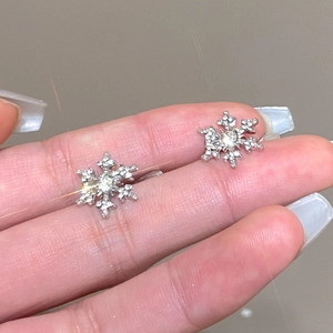 Macro shot of sparkling silver snowflake ear cuff with zircons held on a fingertip