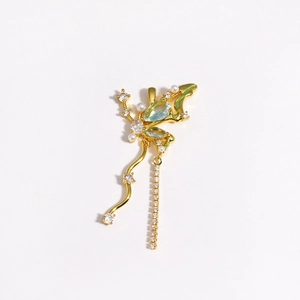 Detail of gold butterfly earring with green gems, pearls and dangling rhinestone chains