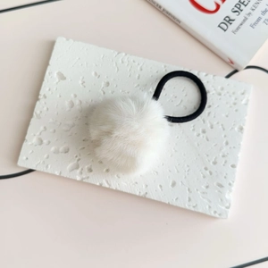 Detailed view of a soft white plush pom pom hair tie with high elastic black cord