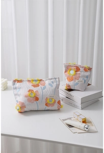 Macro detail of 3D floral embroidery and fabric texture on a soft grey cosmetic bag