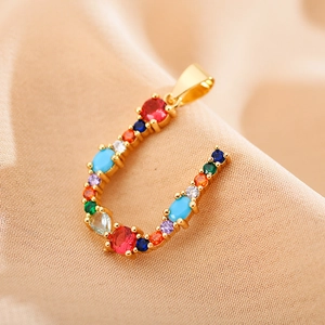Macro shot of gold letter U pendant with colorful zircon stones on champagne fabric
