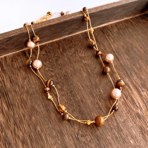Detail of double-strand tiger eye beaded necklace with pearls on a rustic wood background