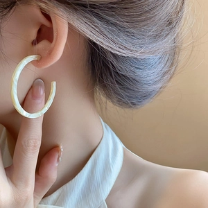 Detailed close-up of retro C-shaped marble resin earrings worn for a French elegant look