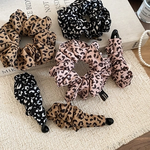 Detailed view of leopard print scrunchies and hair clips on textured fabric with book