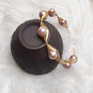 Detailed wire-wrapped gold bracelet featuring pink freshwater pearls on a ceramic jar