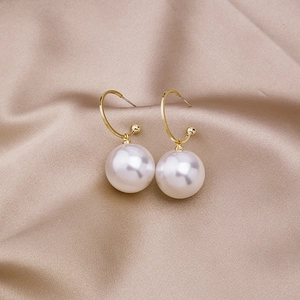 Detailed view of elegant white pearl earrings with golden metal hooks on silk cloth