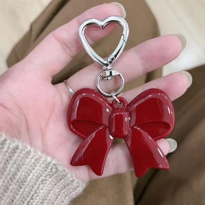 Close-up of a glossy red acrylic bow keychain with a silver heart-shaped metal clip
