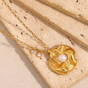 18K vergoldete Kette mit unregelmäßigem Blumenanhänger und Perle auf Steinoberfläche