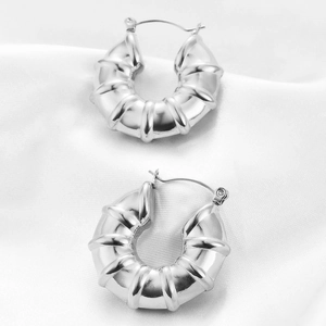 Macro shot of silver U-shaped ridged earrings on white silk with a polished finish