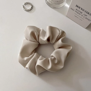 Detail of elegant champagne satin silk scrunchie with soft folds and minimalist props