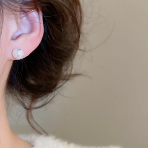 Close-up of elegant round pearl earrings with a lustrous white finish on model's ear