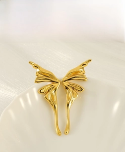 Detailed close-up of golden butterfly wing earrings with polished finish on a white shell