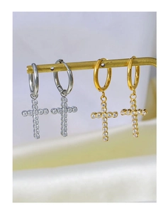 Detailed view of silver and gold cross pendant earrings with cubic zirconia on a silk backdrop