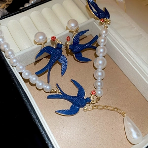 Detail of blue swallow and pearl necklace and earring set in a beige jewelry box