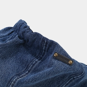 Detailed view of elastic denim waistband with branded leather tag and brass rivets