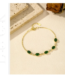 Detail of elegant gold bracelet with green emerald-cut stones and clear zircons