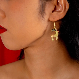 Close-up of golden Christmas reindeer earrings worn on ear against red backdrop
