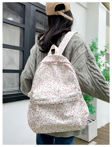 Detailed view of floral canvas backpack on a model wearing a grey knit sweater