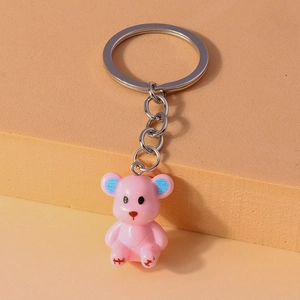 Close-up of pink resin bear keychain with blue glitter ears on a beige background